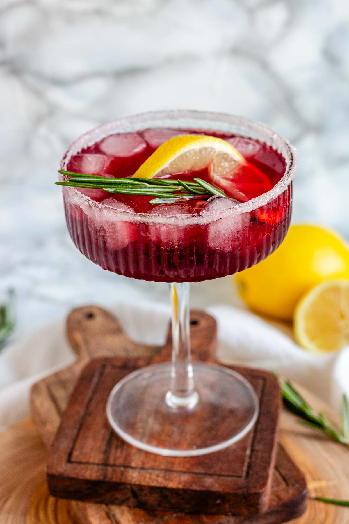 Pomegranate vodka cocktail in a coupe glass with rosemary and a lemon slice.