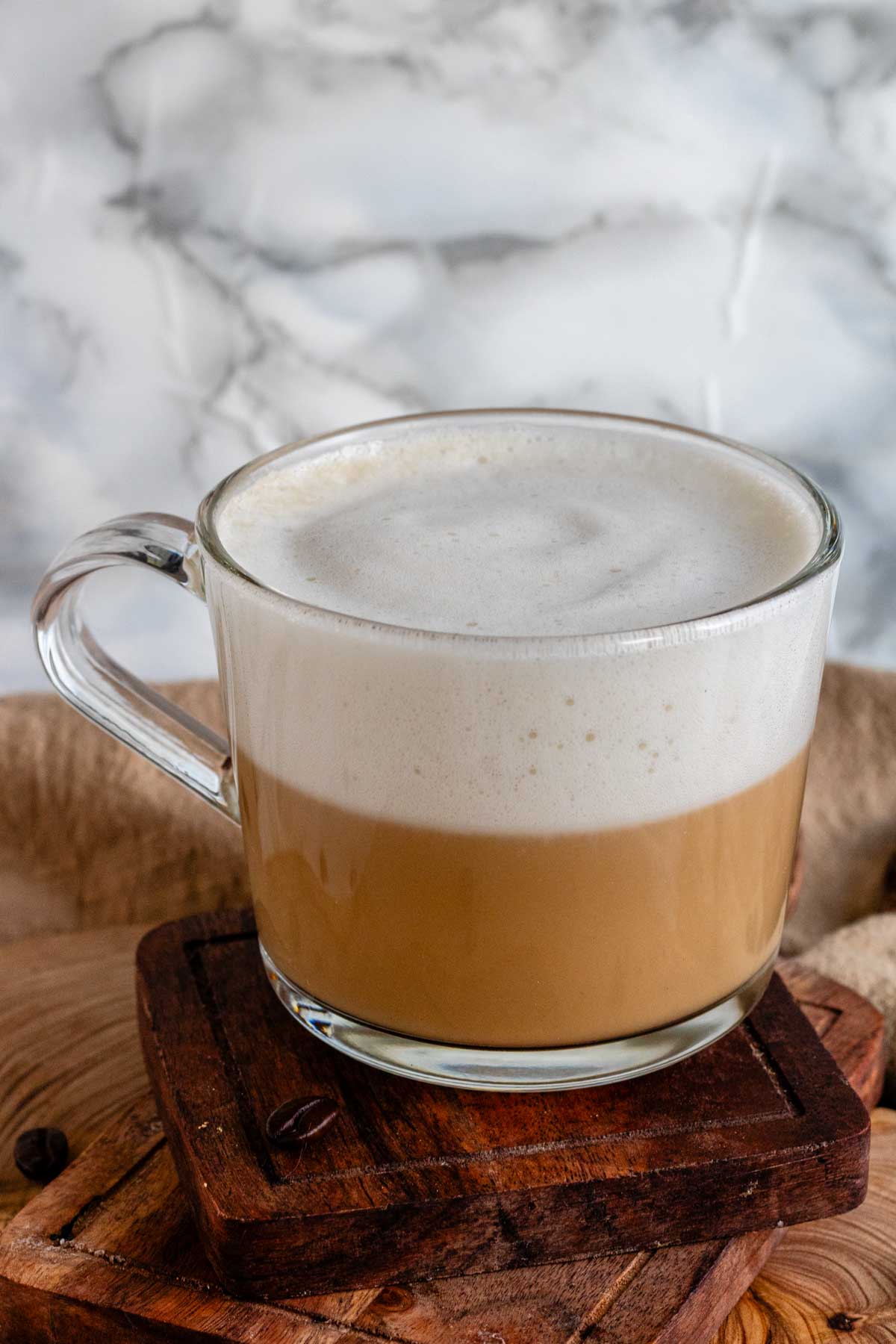 Vanilla oat latte in a glass mug on a wooden board.