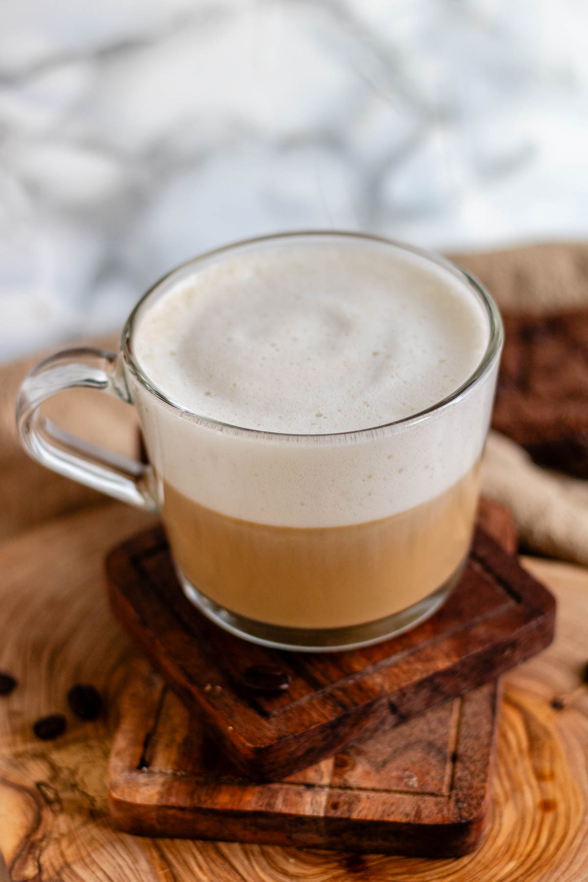 Vanilla oat latte in a glass mug on a wooden board.