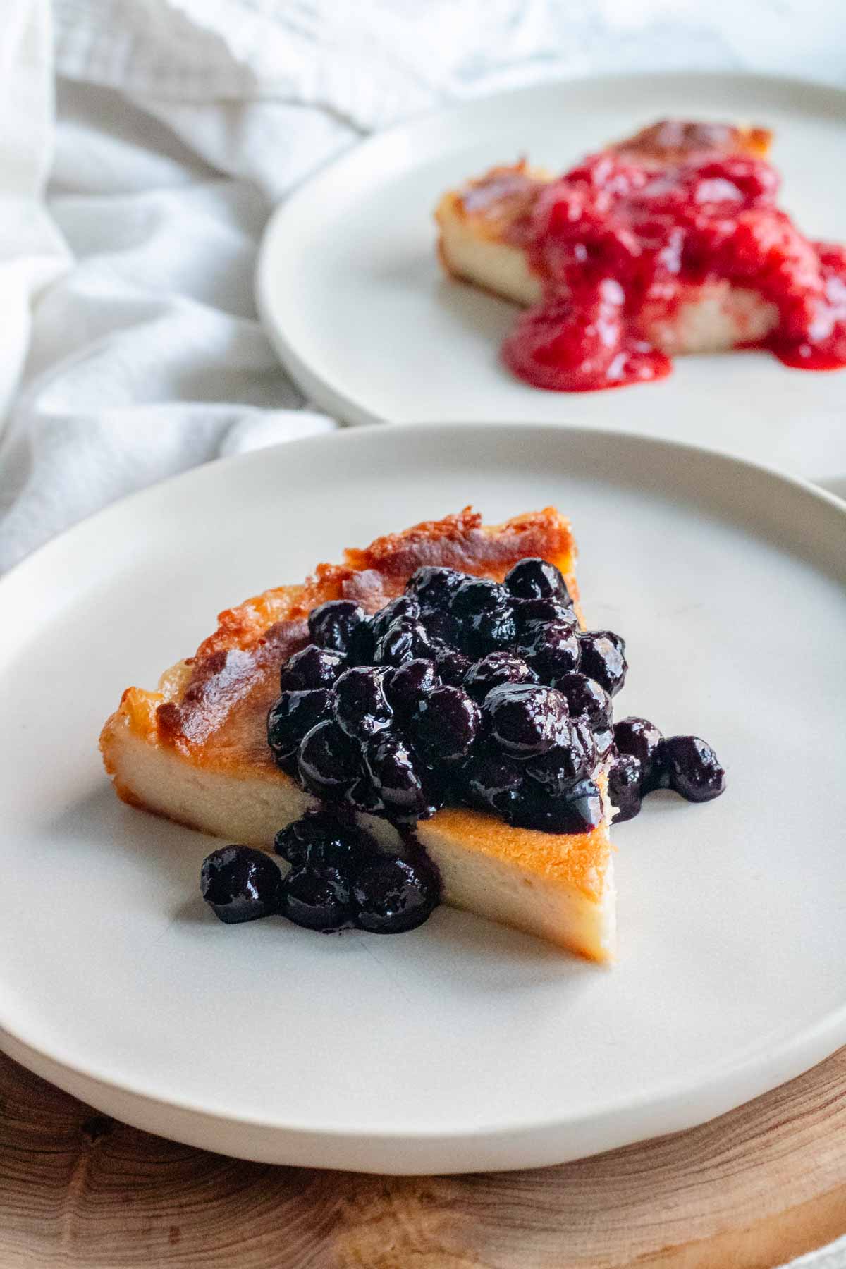 Two vegan cheesecake slices with blueberry sauce and strawberry sauce.