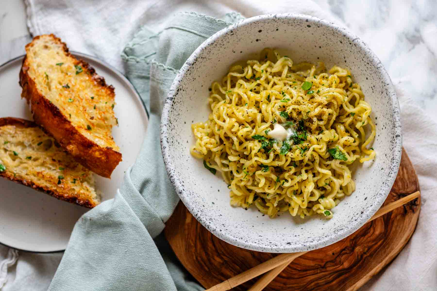 Vegan buttered noodles in a white bowl with garlic toast.