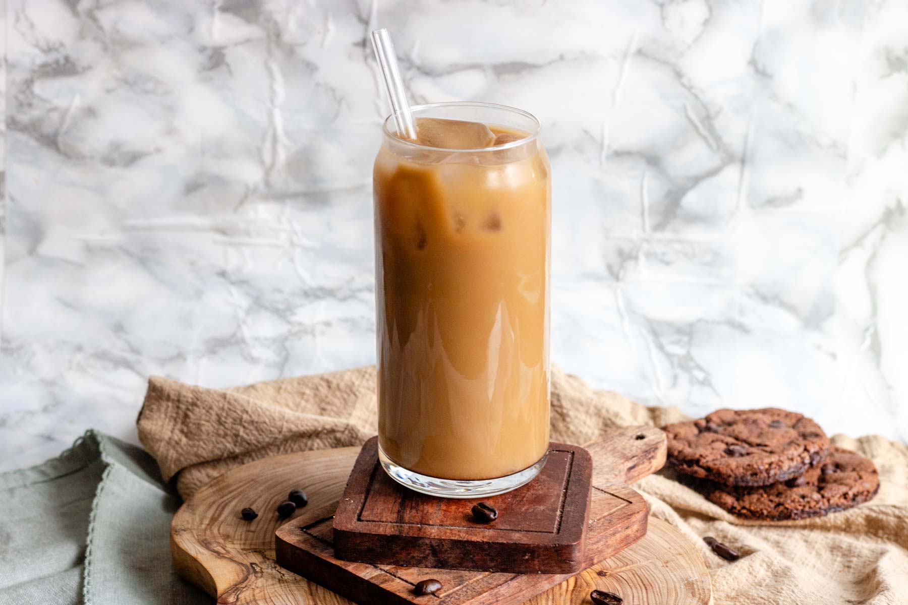 Vegan cold coffee in a glass with a straw on a wooden board.