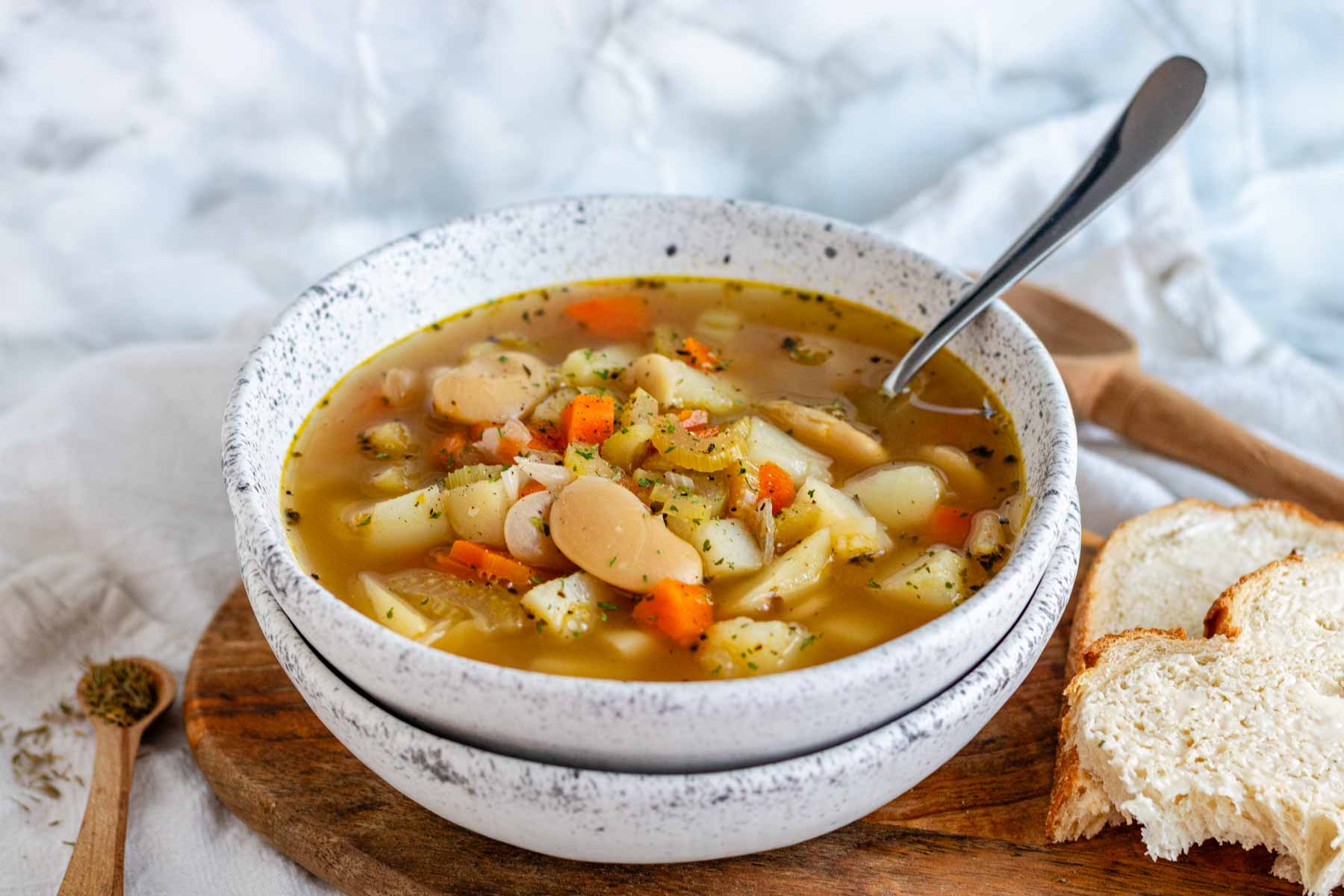 A bowl of lima bean soup with a spoon and bread.