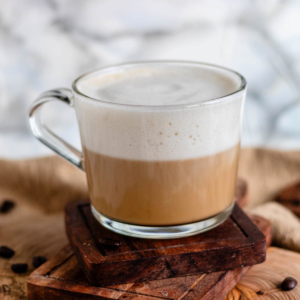 Vanilla oat latte in a clear mug on a wooden board.