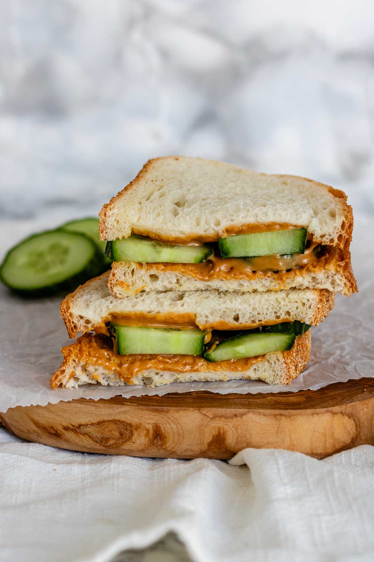 Peanut butter cucumber sandwich cut in half on parchment paper and a wooden board.