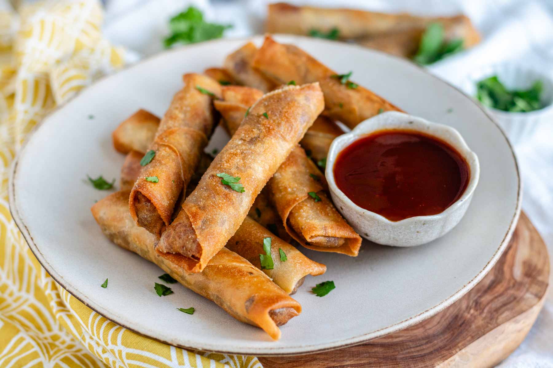 Vegan lumpia on a plate with sauce and cilantro.
