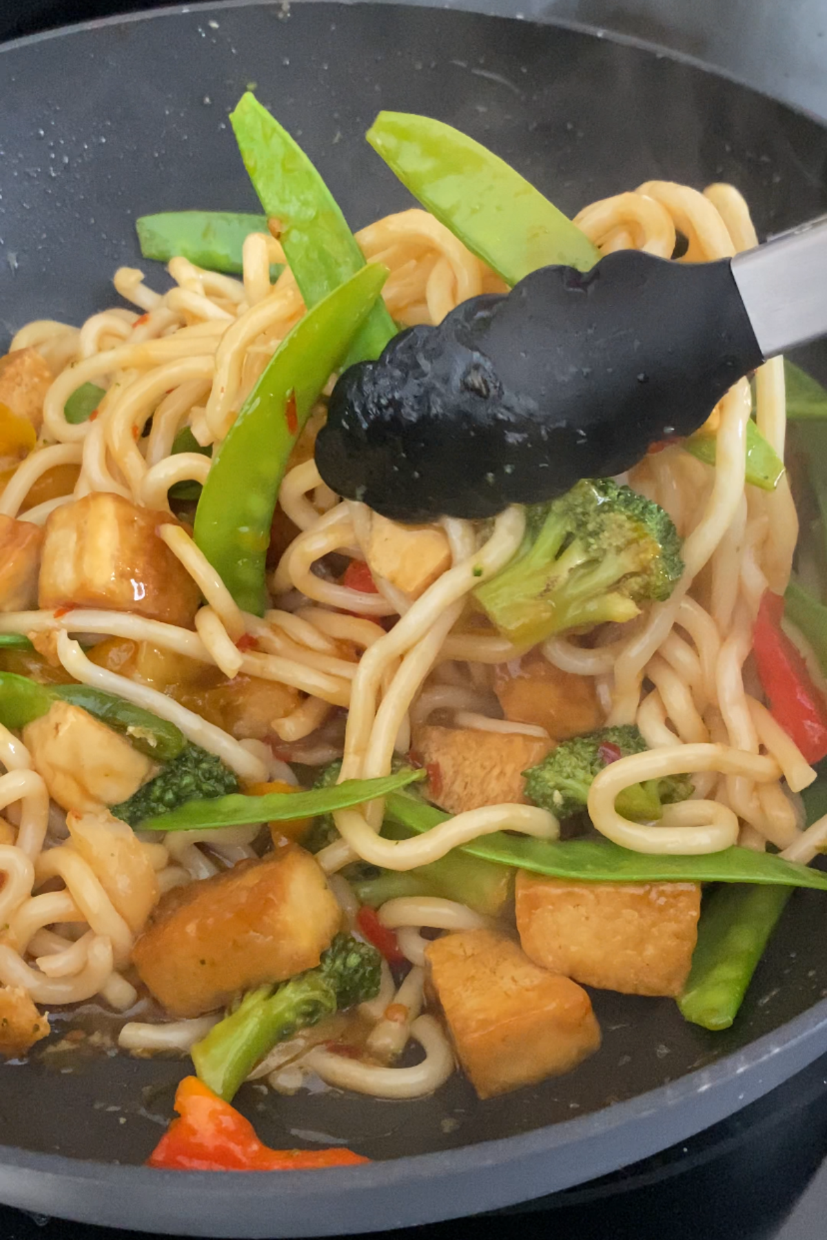 Mixing tofu udon stir fry in a wok.