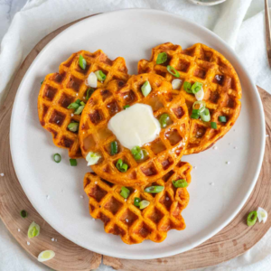 Four sweet potato waffles on a plate with butter and green onion.