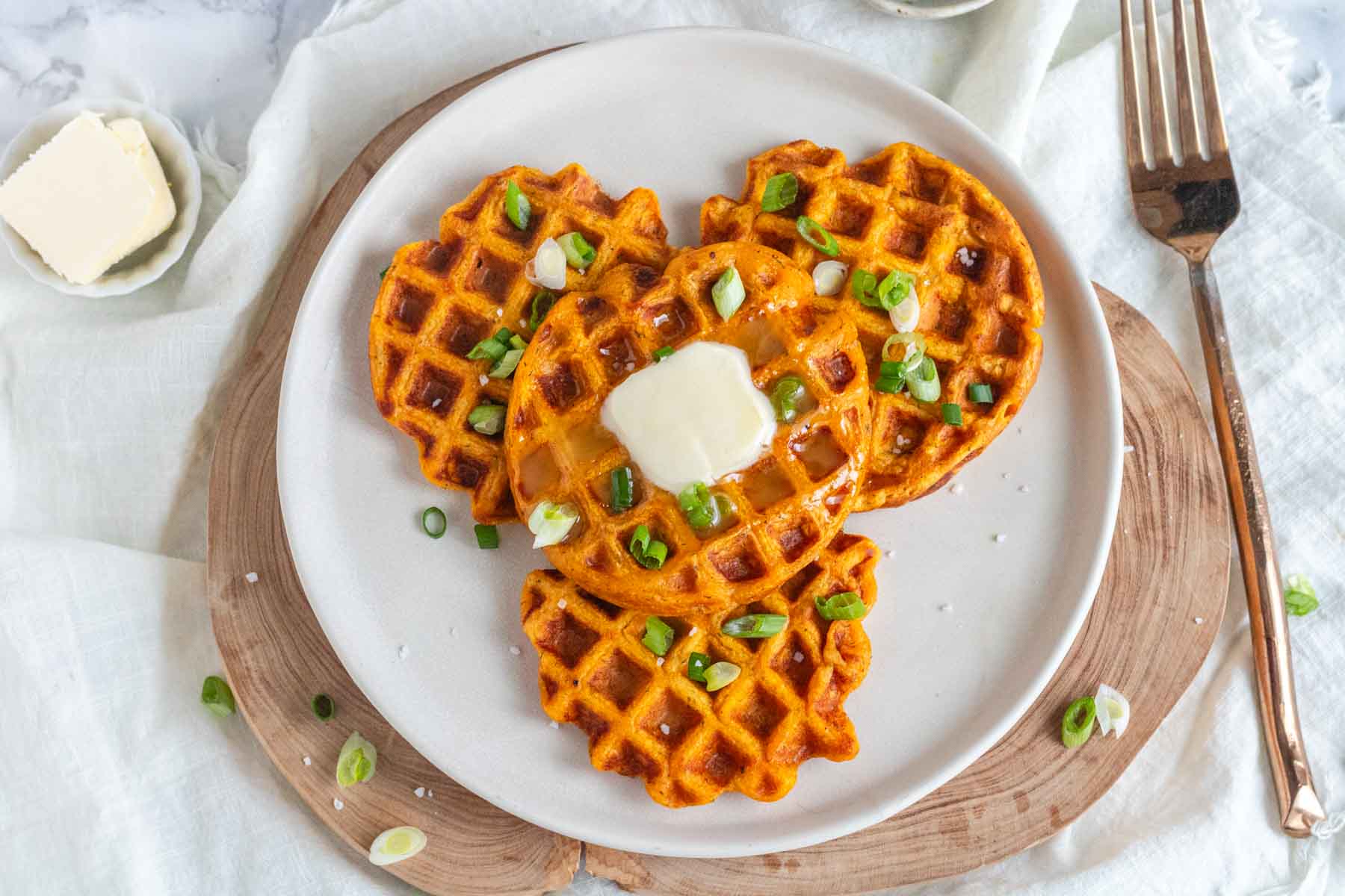 Four sweet potato waffles on a plate with butter and green onion.