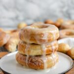 Three glazed donuts stacked on a white plate.