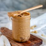 A jar of cashew butter and a wooden spoon on a wooden board.