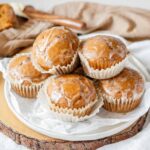 Glazed muffins piled on a parchment paper lined plate on a wooden board.