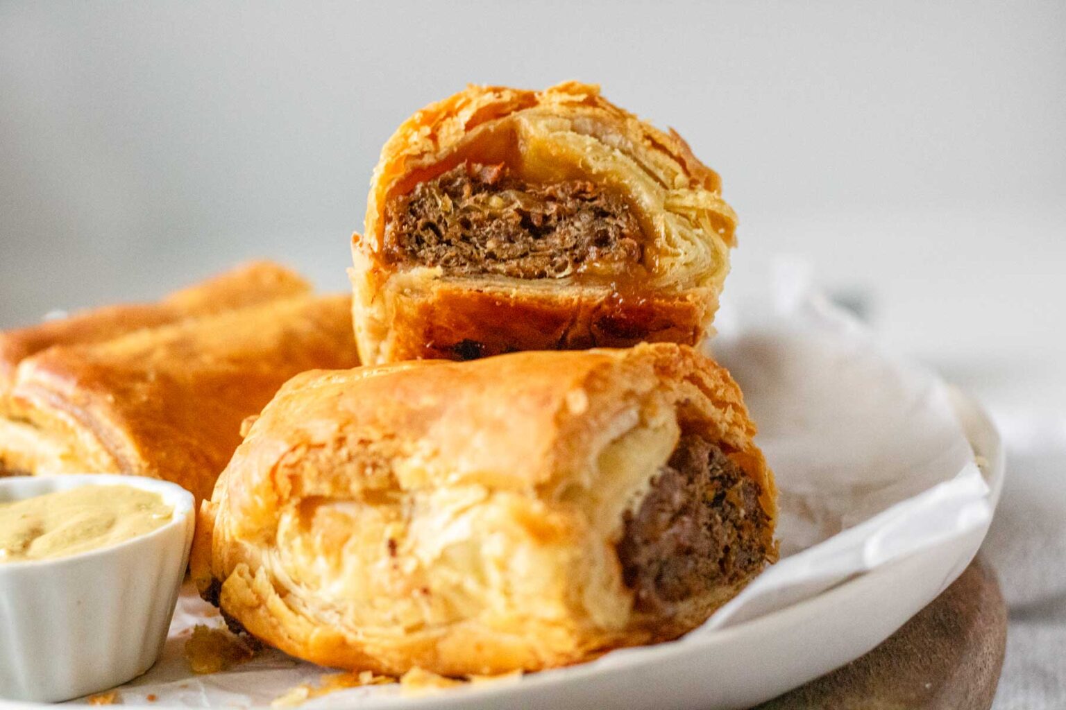Golden-brown flaky pastry filled with savory meat, cut in half to reveal the textured filling, served with a small bowl of mustard.