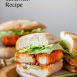 A buffalo tofu sandwich with lettuce on a white plate with pickles, with black text above.
