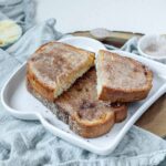 A slice of cinnamon toast cut in half on a whole piece of cinnamon toast, on a white plate.