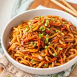 Teriyaki udon noodles topped with green onions in a light grey bowl.