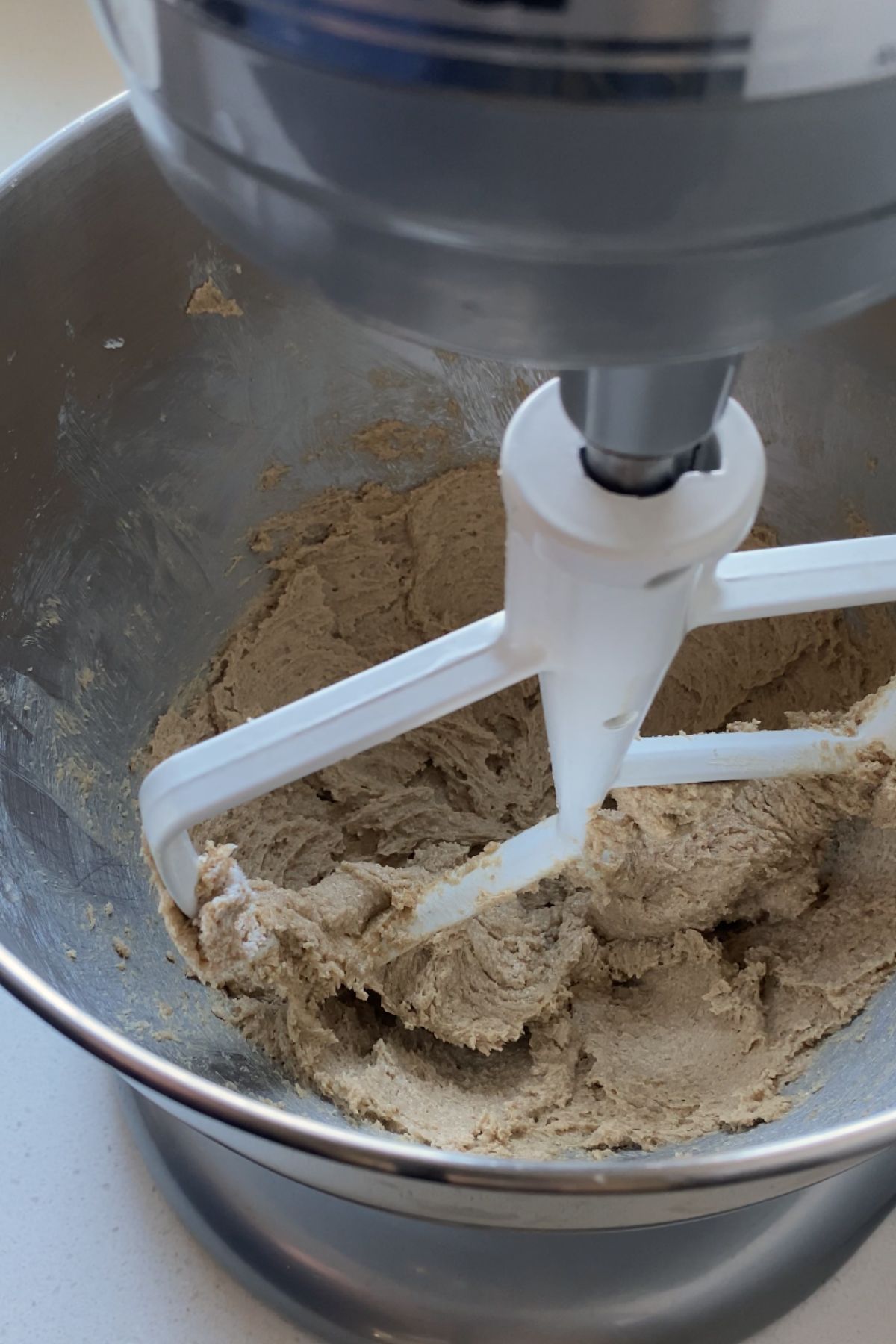 Creamed butter and brown sugar in a stainless steal stand mixer with a white mixer attachment.