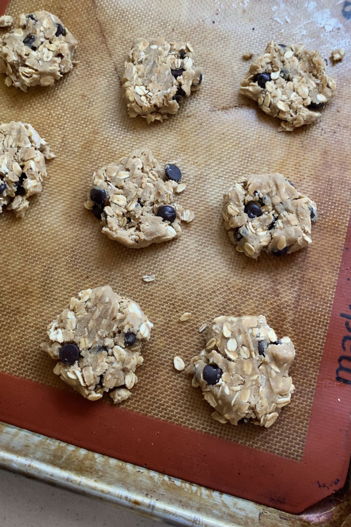 Flattened vegan oatmeal chocolate chip cookie dough balls on a silicone baking mat.