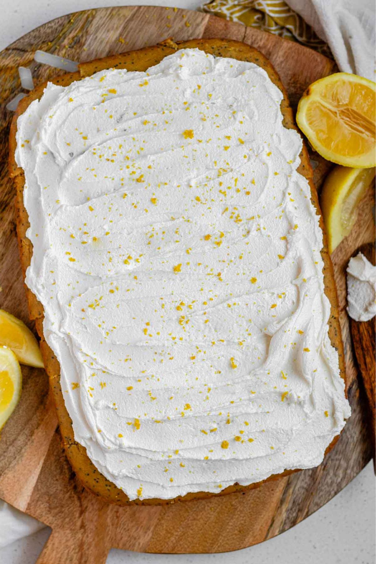 A top down view of frosted lemon poppy seed cake on a wooden board.