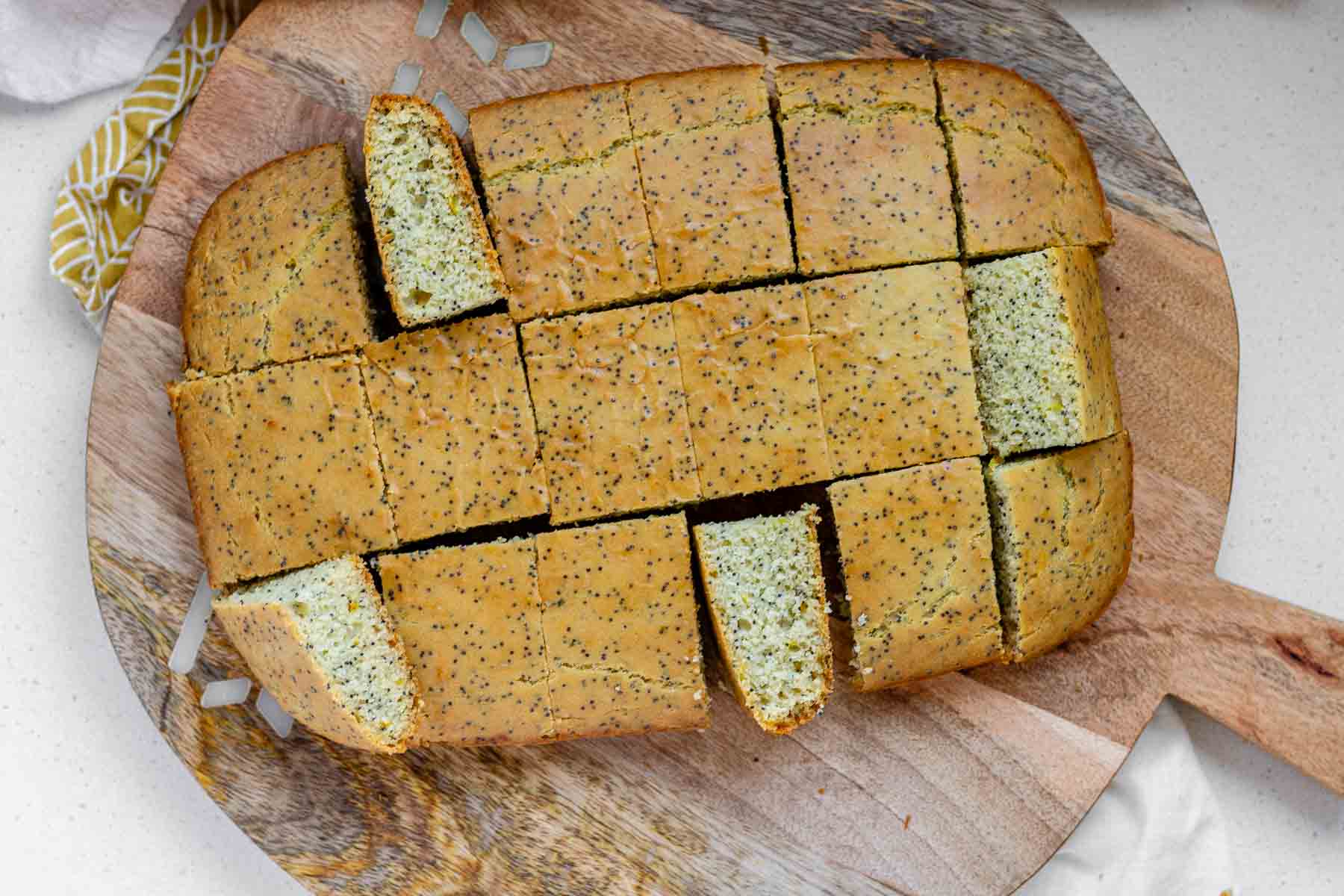 Unfrosted lemon poppy seed cake sliced into squares with some turn on their sides to show the crumb.