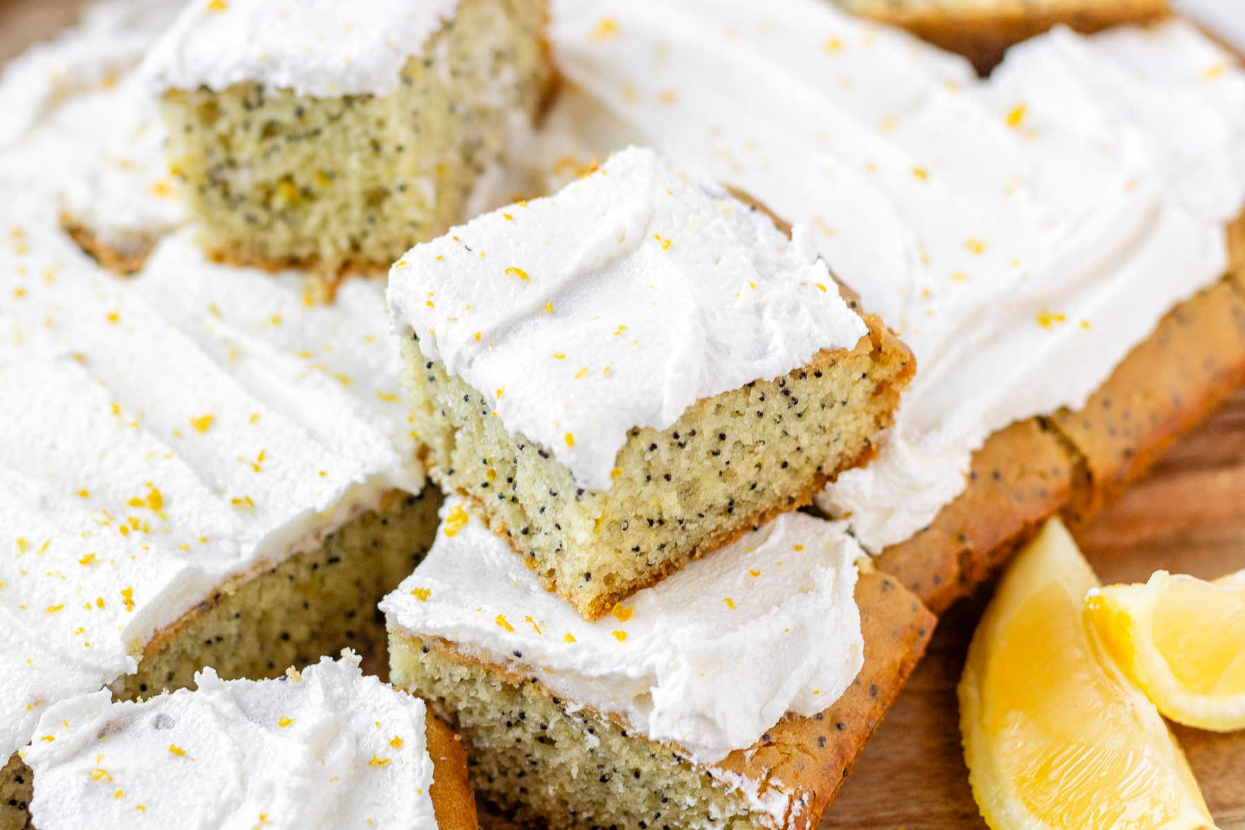 Lemon poppy seed cake squares stacked on a wooden board.
