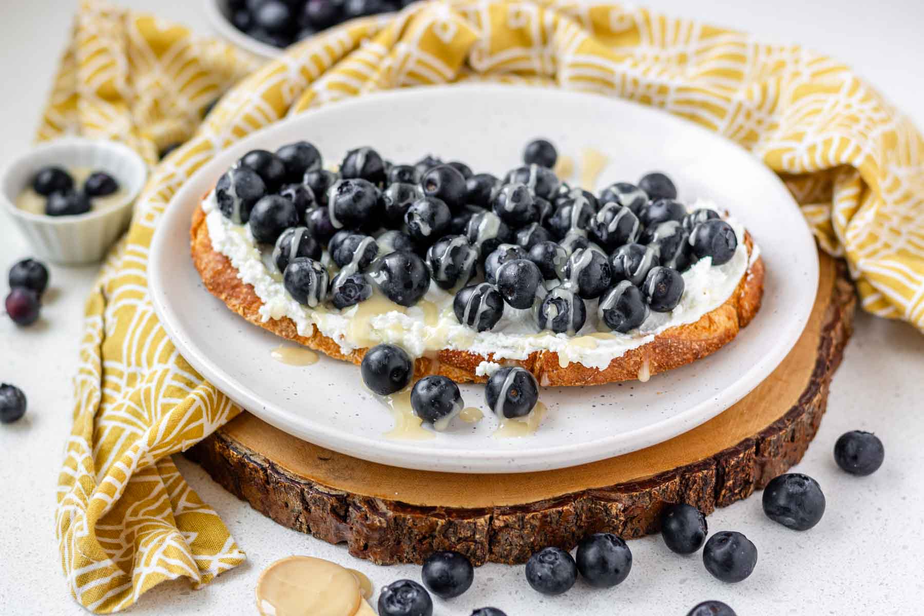 Blueberry goat cheese toast on a white plate on a wooden platter.