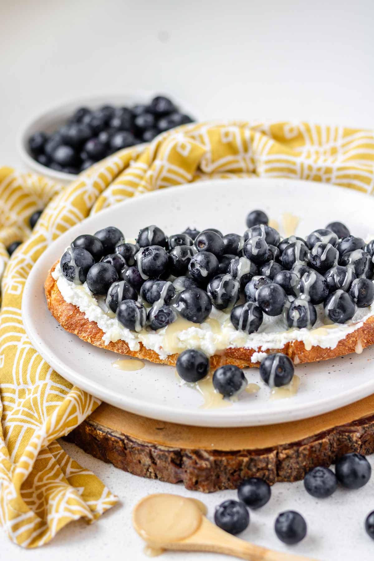 Blueberry goat cheese toast on a white plate on a wooden platter.