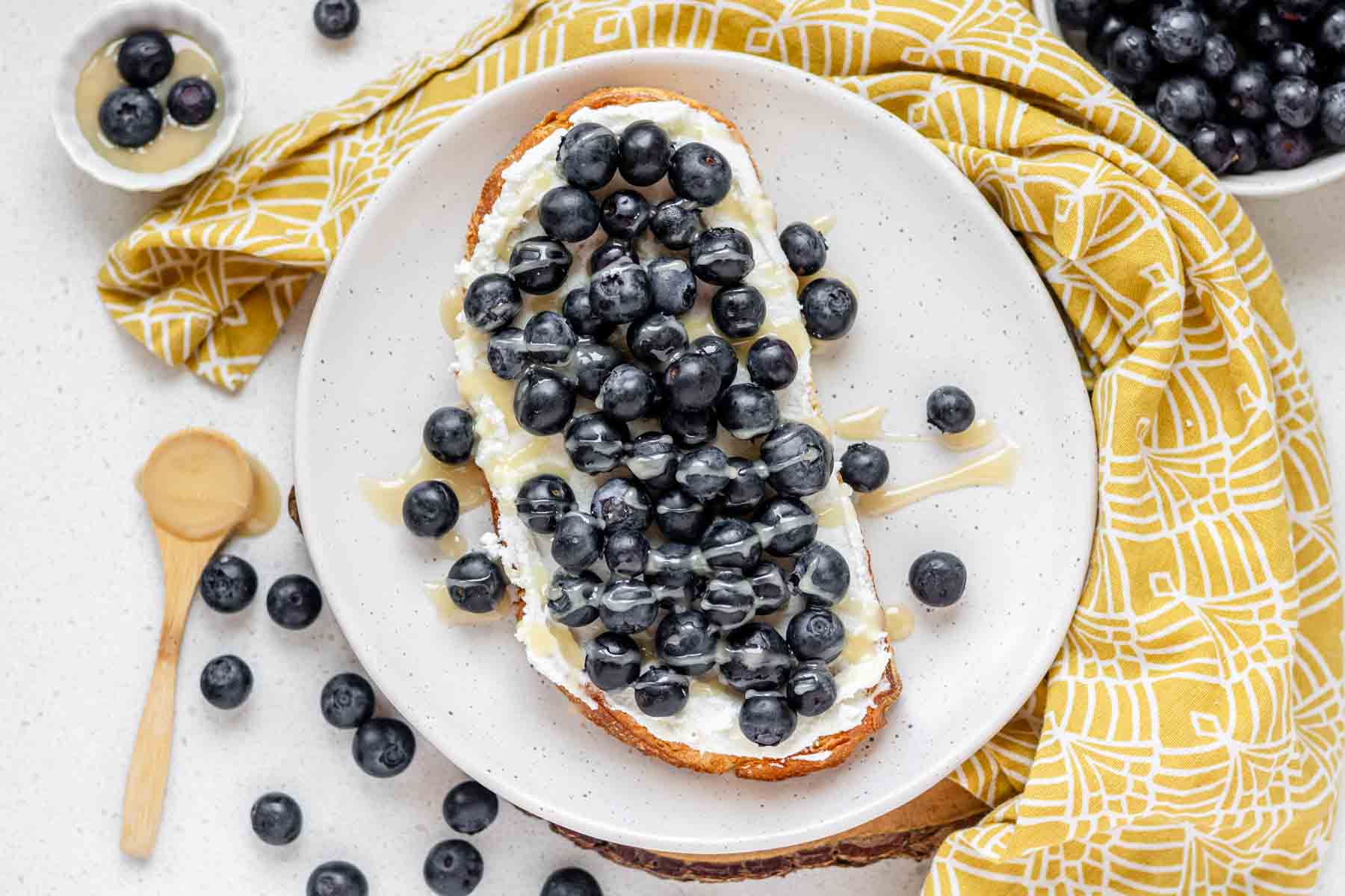 A top down view of toast topped with goat cheese, blueberries and honey.