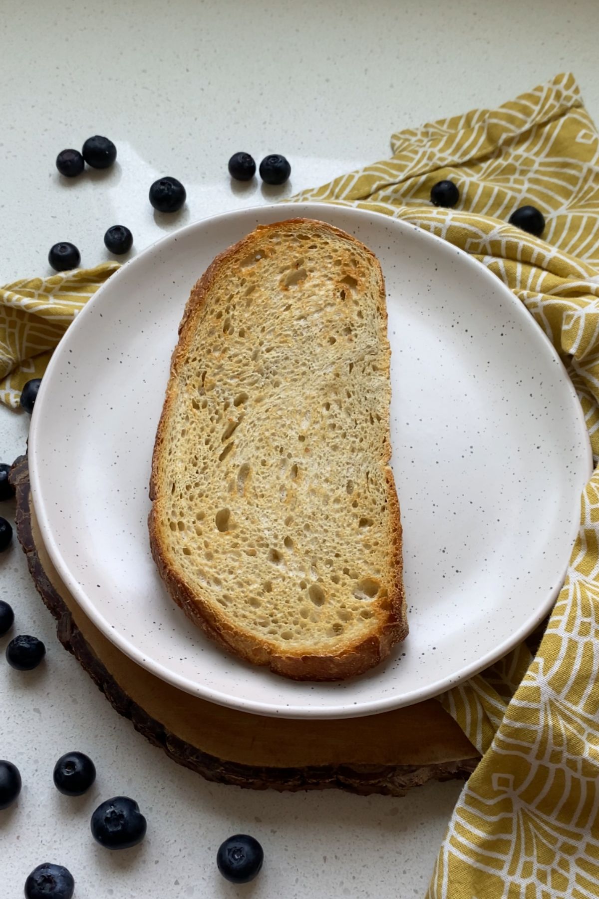 A piece of toast on a white plate with a white and yellow cloth napkin.