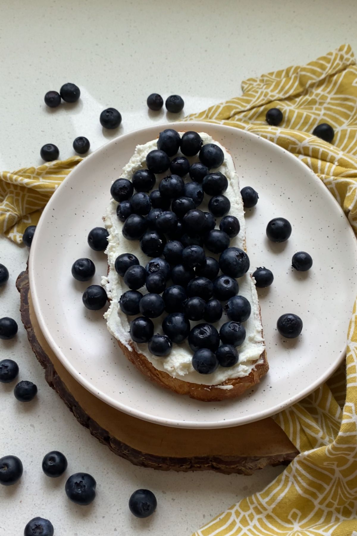 A piece of toast spread with goat cheese and topped with blueberries.