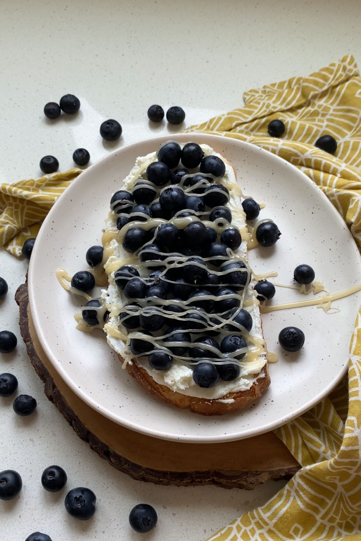 A piece of toast topped with goat cheese, blueberries and honey on a white plate.