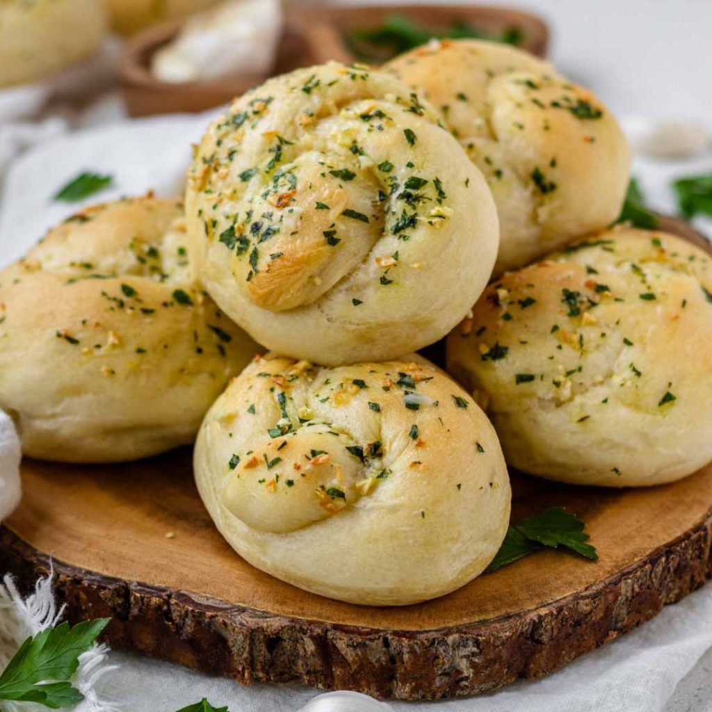 Vegan garlic knots piled on a circular wooden board.