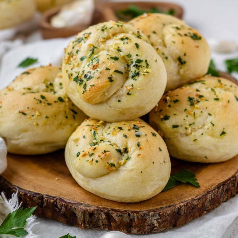 Vegan garlic knots piled on a circular wooden board.
