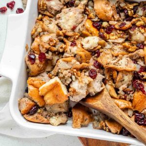 Stuffing with walnuts and cranberries in a white baking dish with a wooden spoon.