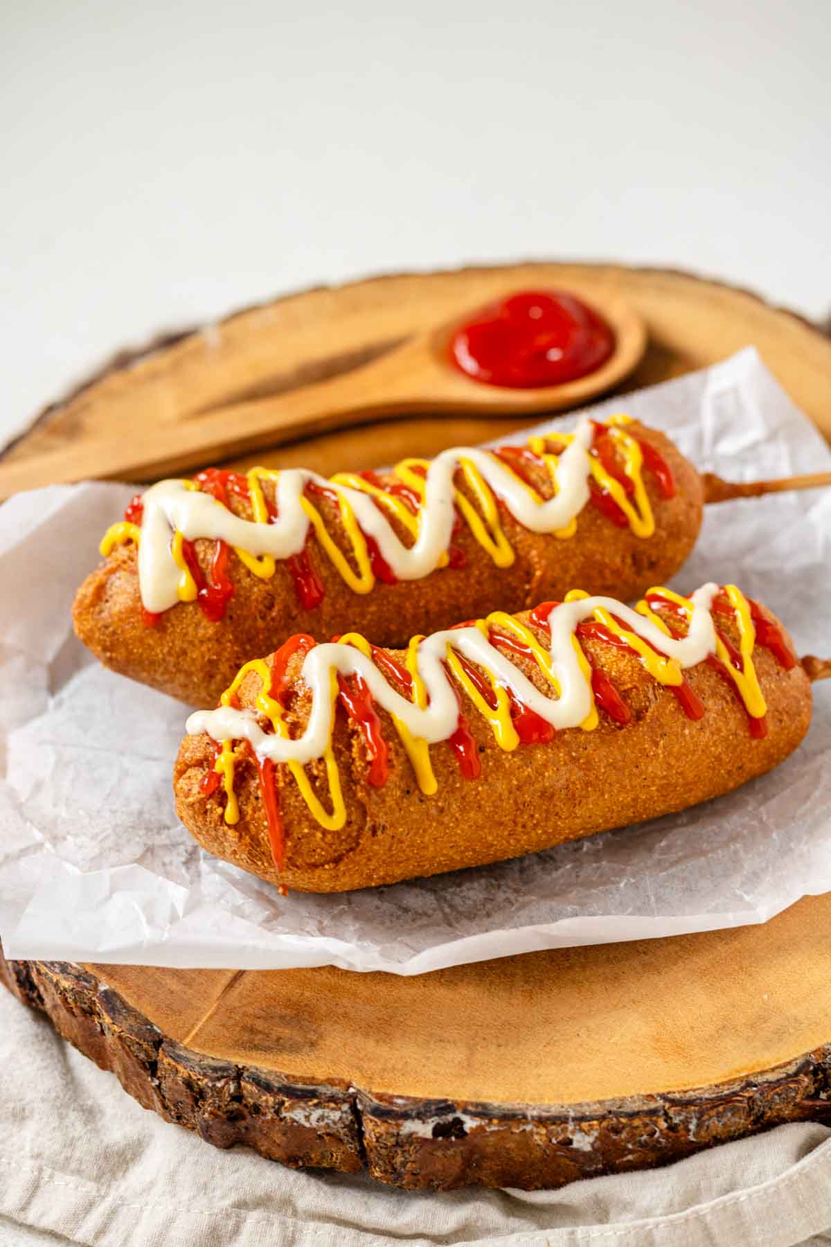 Two vegan corn dogs topped with ketchup, mustard, and vegan mayo on a wooden platter.