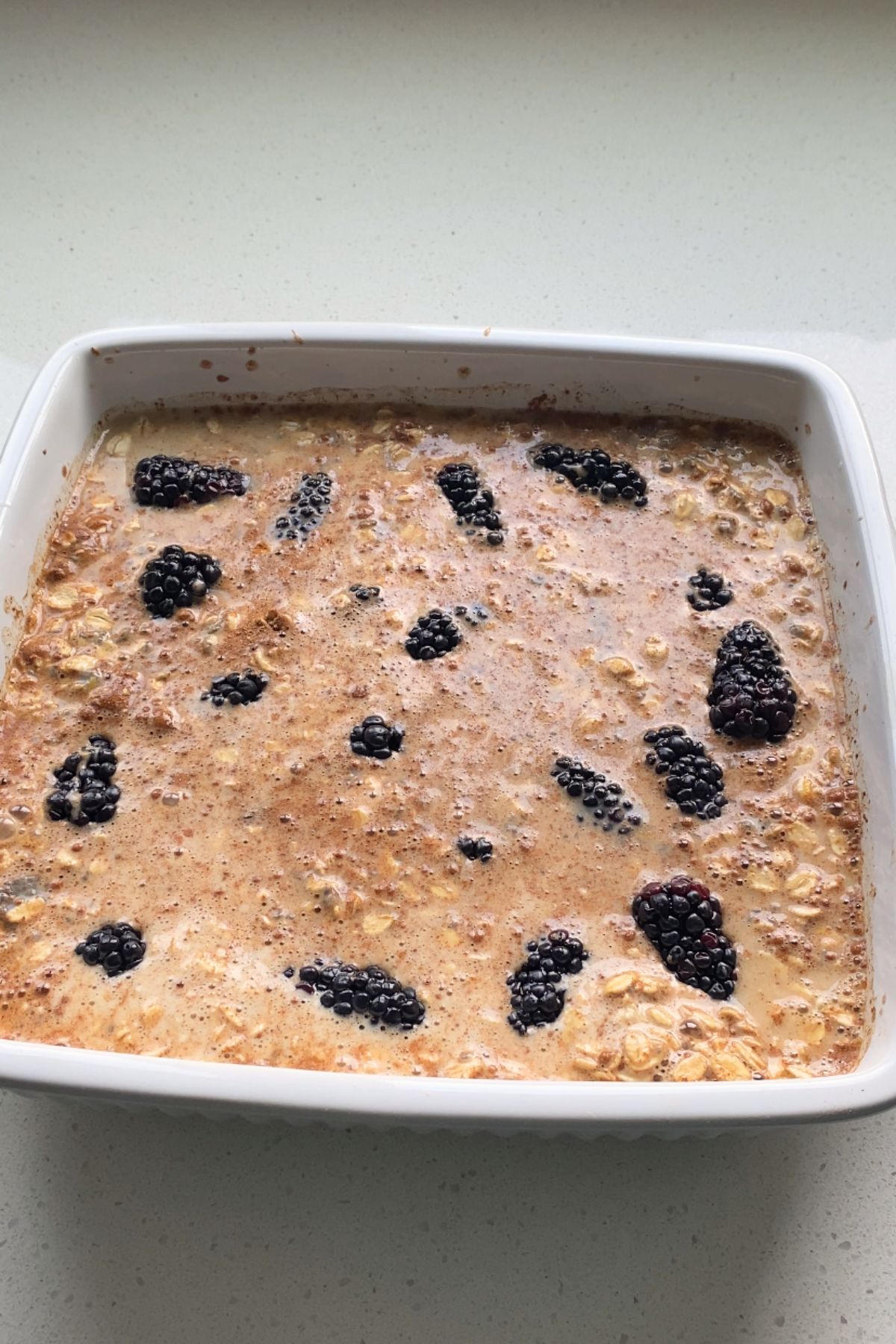 Unbaked oatmeal mixture with blackberries in a white baking dish.