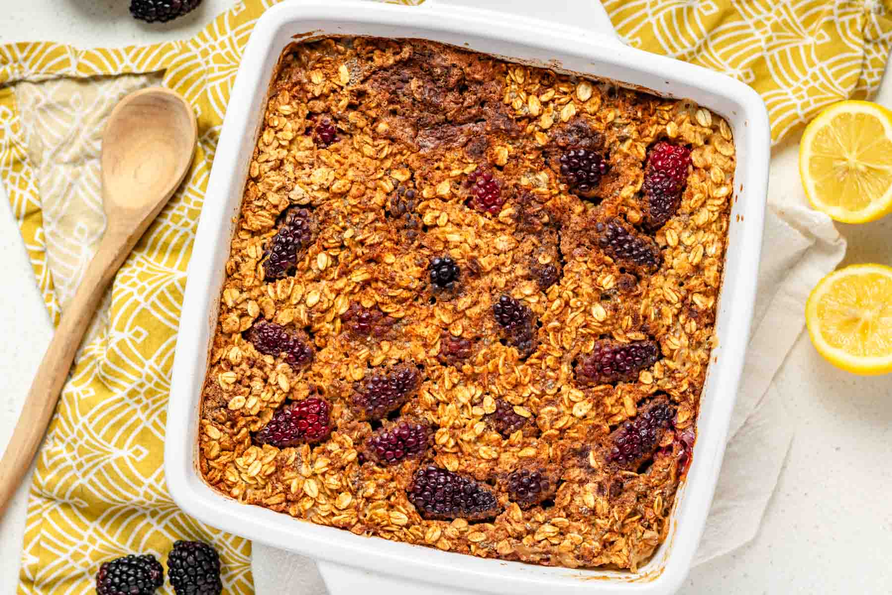 A top down view of blackberry baked oatmeal on a white and yellow cloth napkin and a sliced lemon.