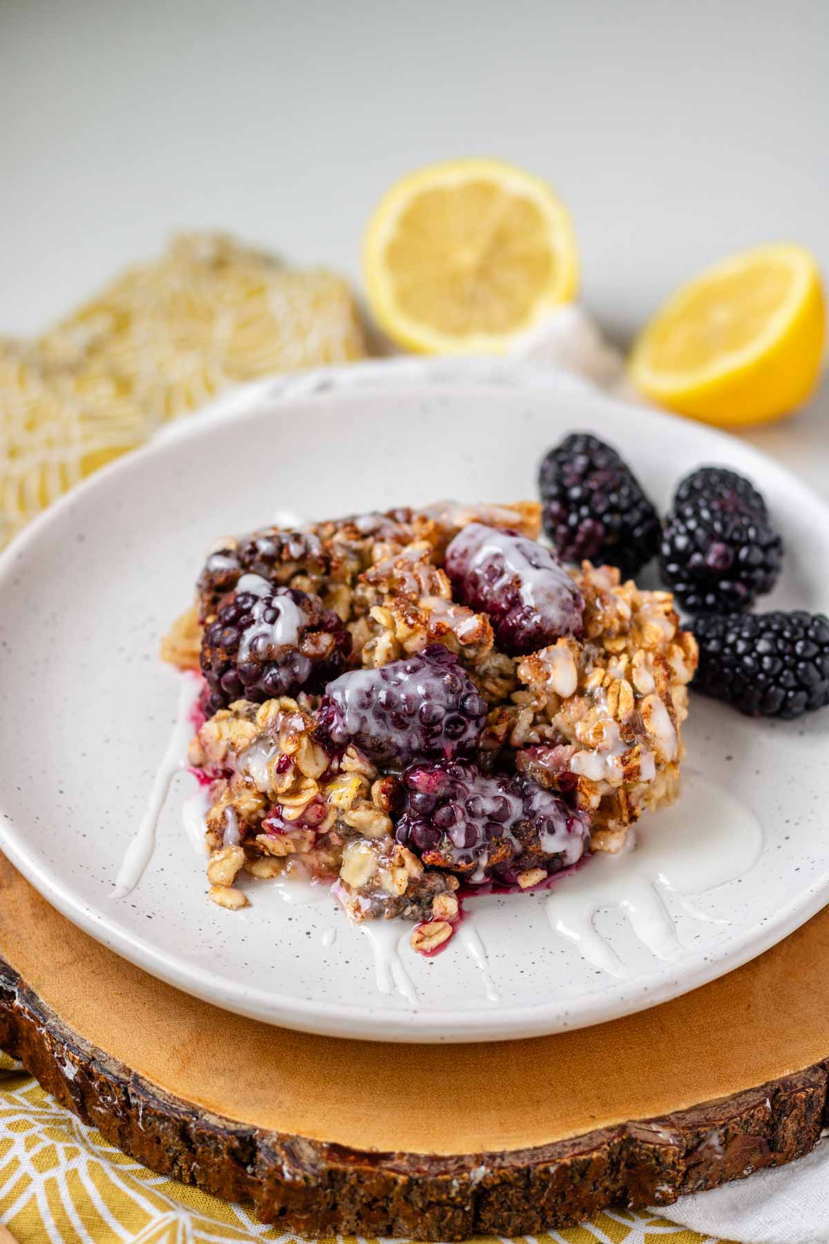 A slice of blackberry baked oatmeal on a white plate topped with glaze.