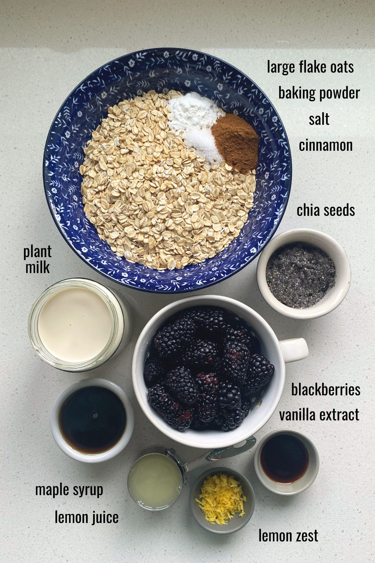 Ingredients for blackberry baked oatmeal in dishes on a white counter top.