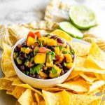 A white bowl of mango black bean salad surrounded by tortilla chips.