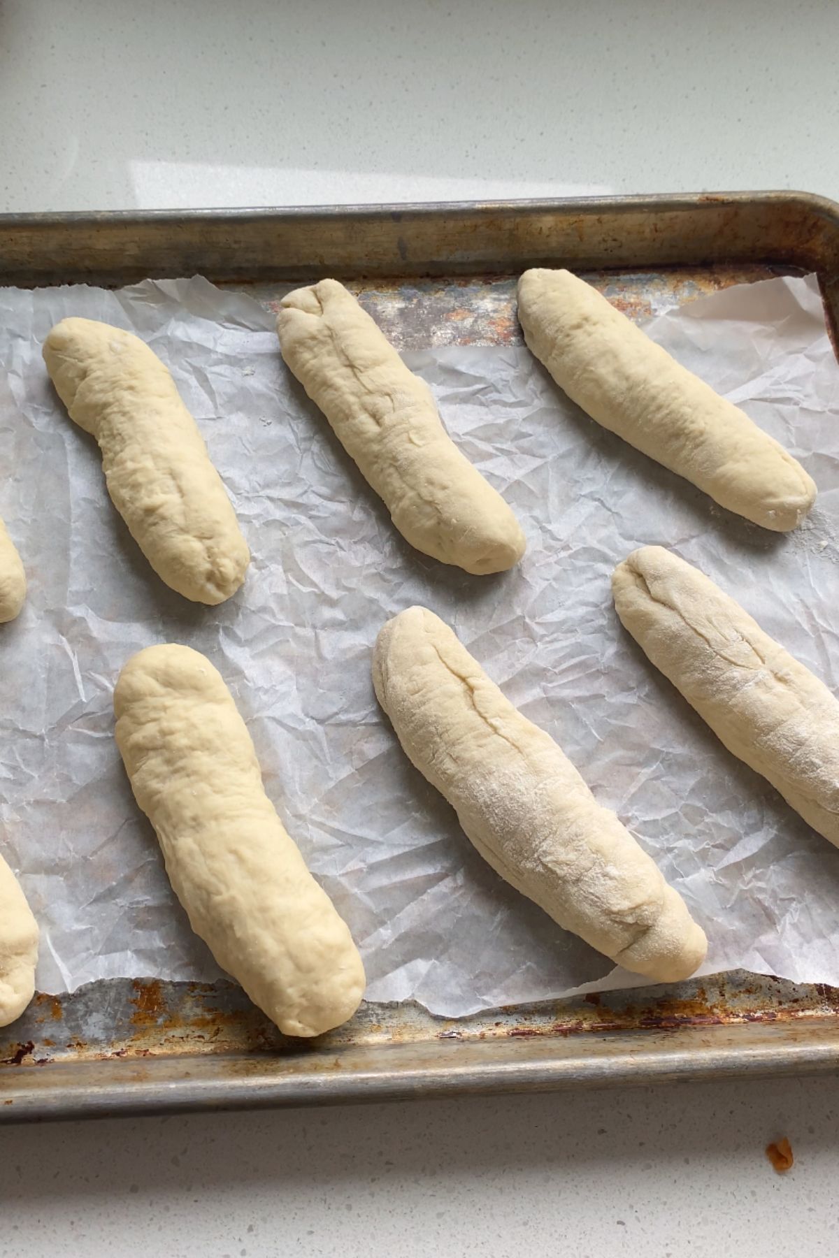 Formed hot dog bun dough on a baking sheet lined with parchment paper.