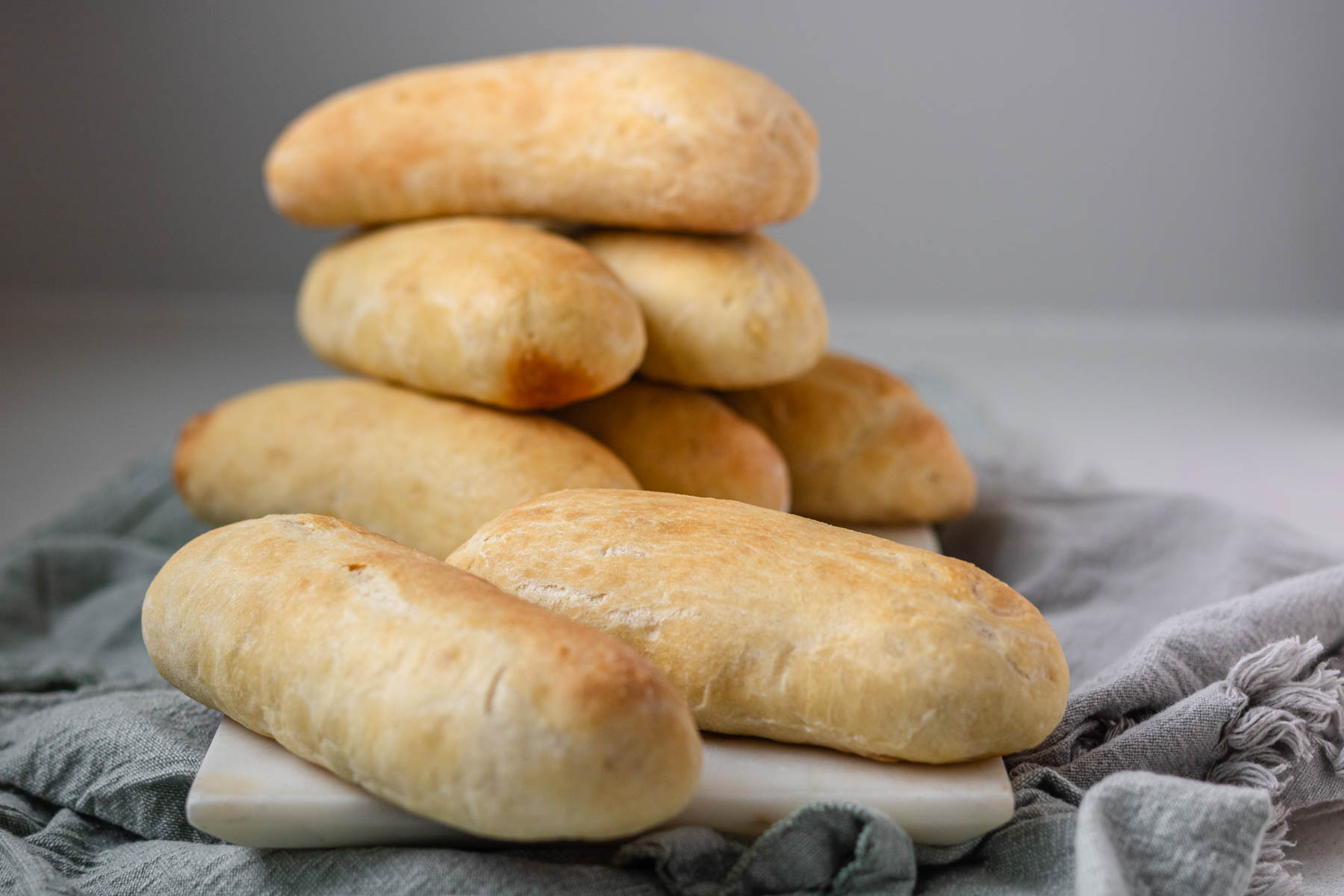 Hot dog buns stacked on a white marble slab with grey cloth napkins.