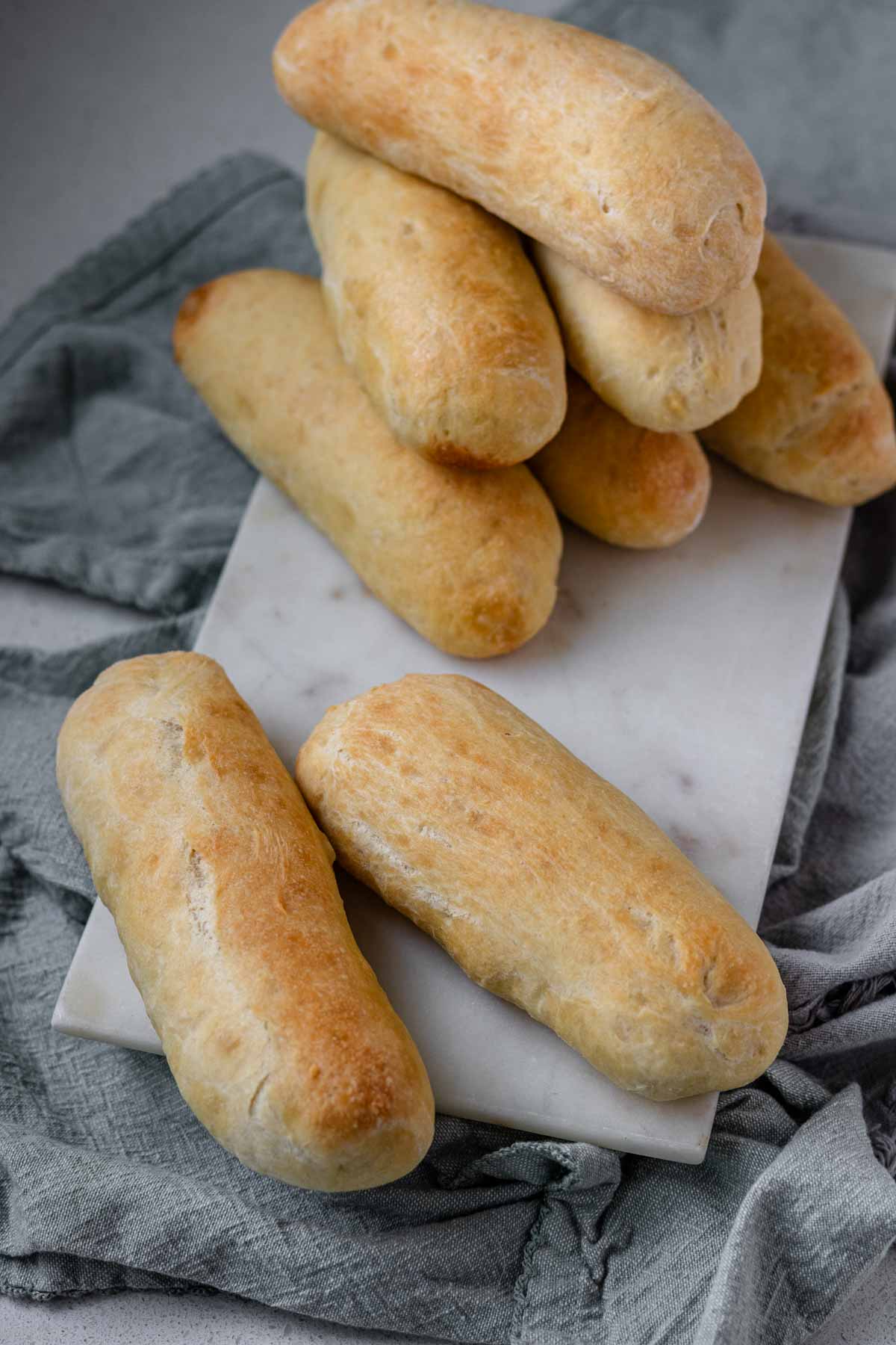 Hot dog buns stacked on a white marble slab.