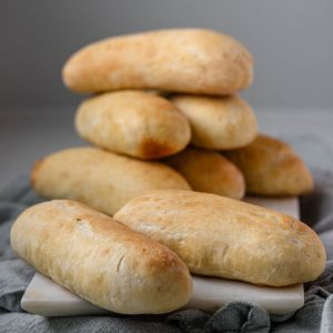 Hot dog buns stacked on a white marble slab.