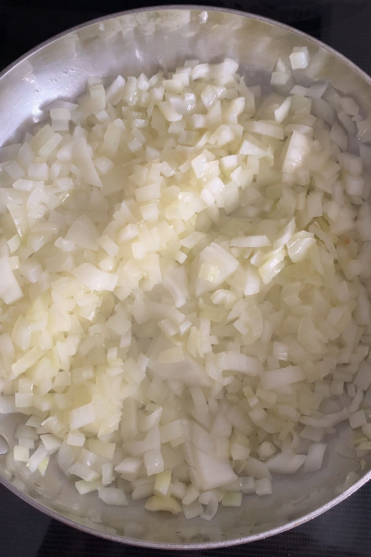 Diced yellow onions cooking in a stainless steel pan.