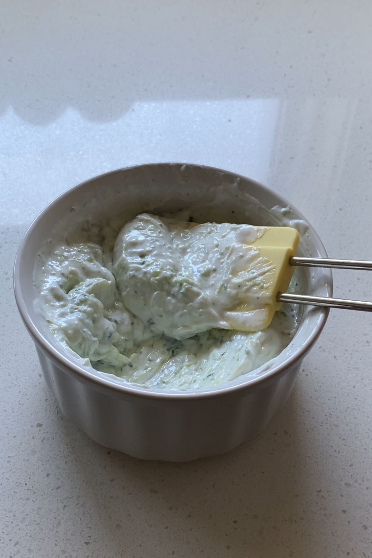 Tzatziki in a small white bowl with a yellow silicone spatula.