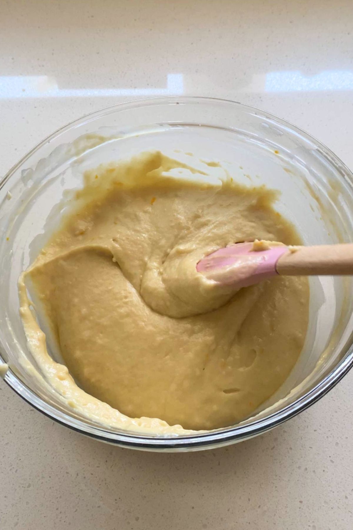 Cake batter in a glass mixing bowl with a pink silicone spatula.