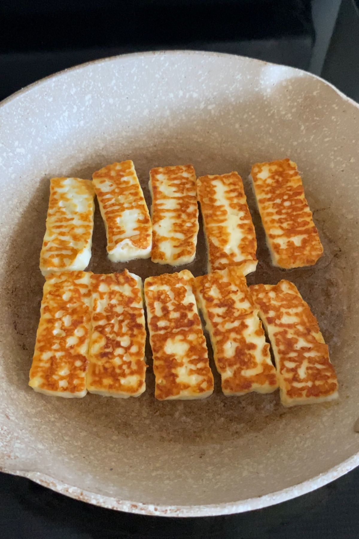 Pieces of grilled halloumi in a beige frying pan.