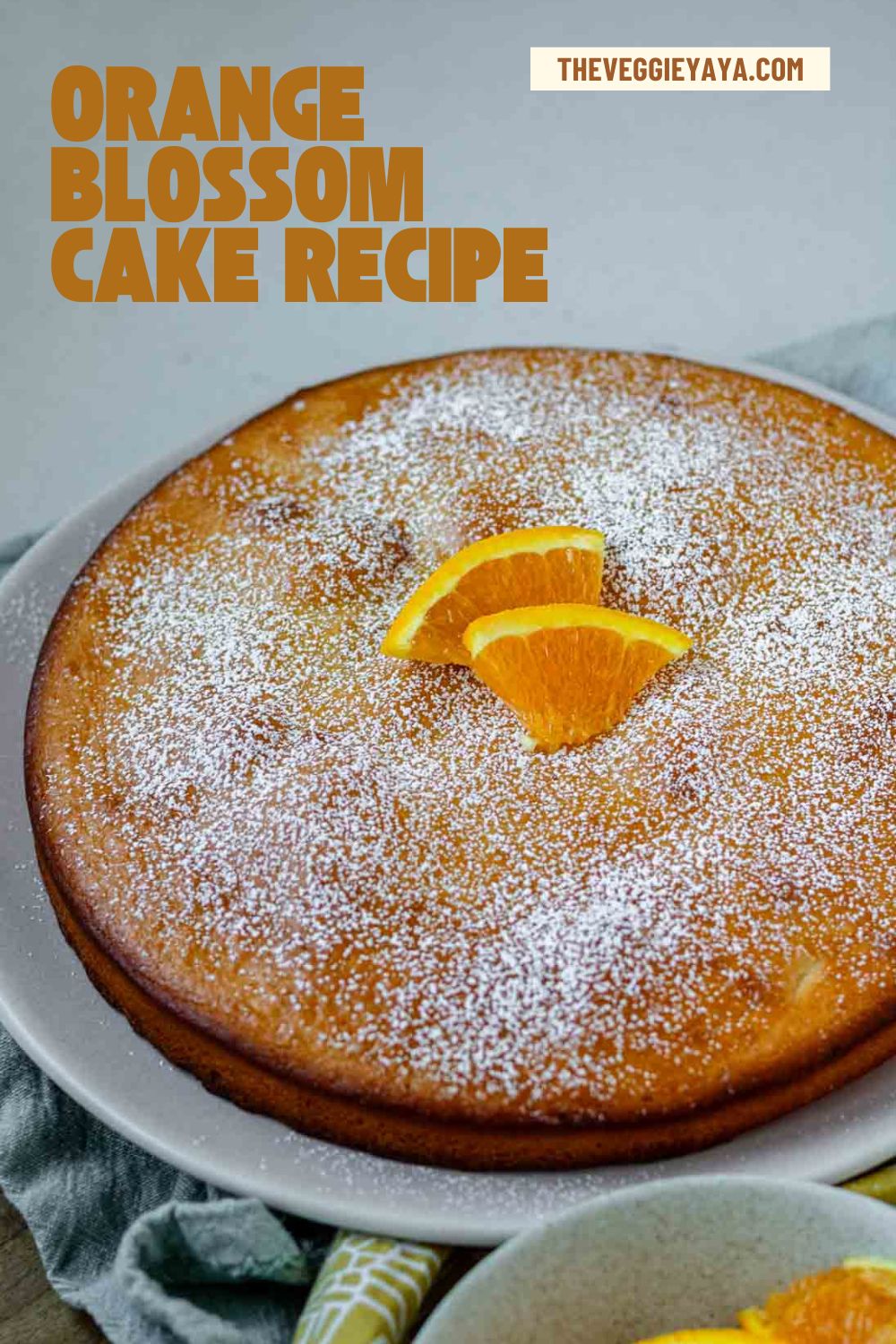 An orange blossom cake topped with powdered sugar with text above indicating the recipe.