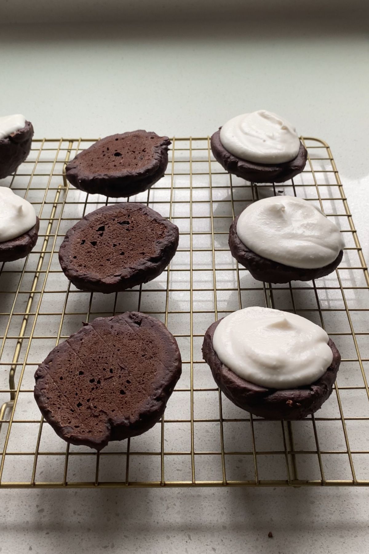 Vegan whoopie pie cakes topped with coconut whipped cream on a cooling rack.